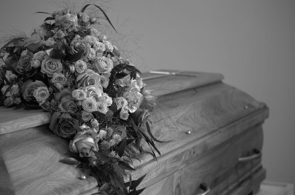 pexels-photo-16350324-16350324 A black and white image featuring a wooden casket adorned with a vibrant floral bouquet, symbolizing respect and memory.