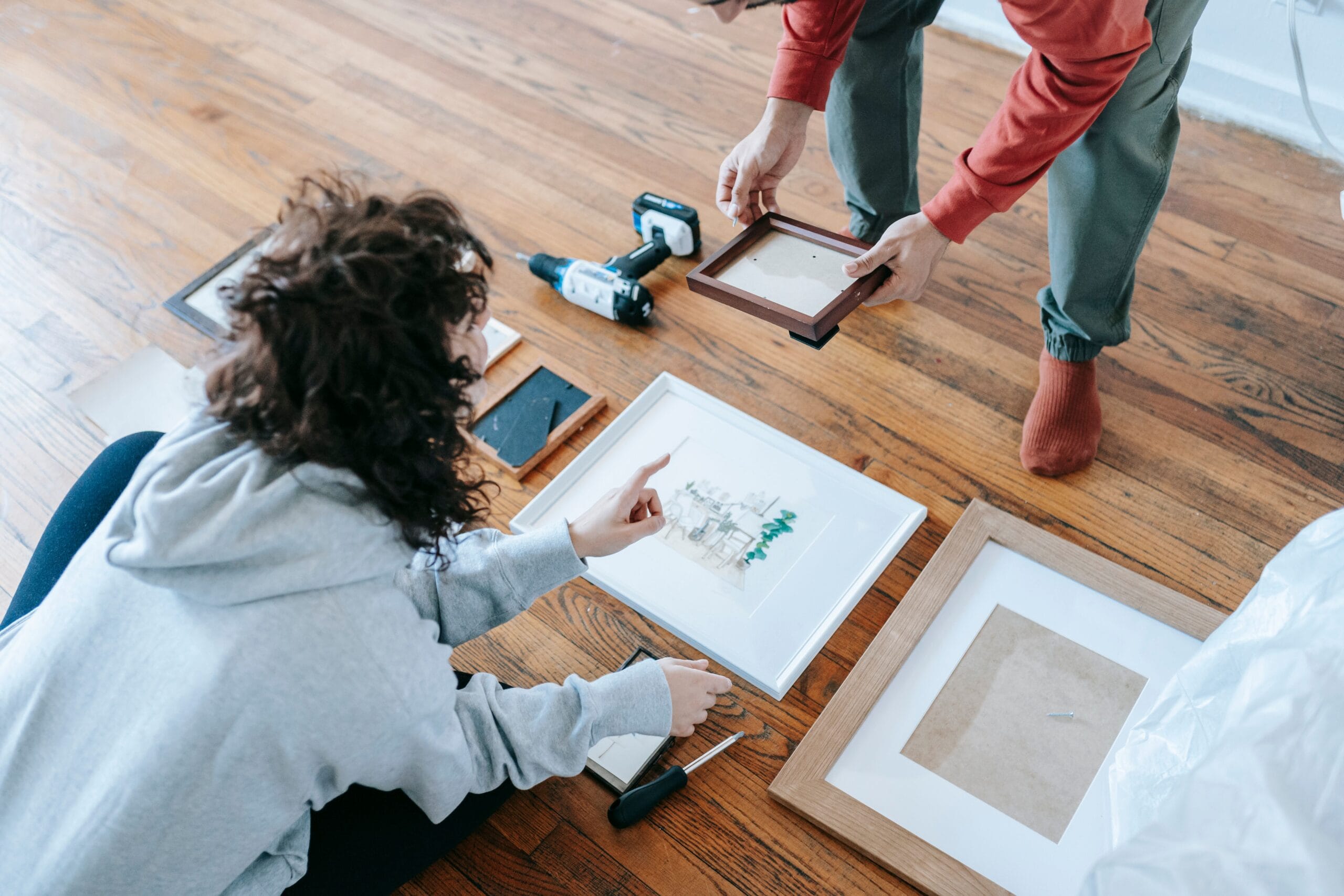 A couple organizing picture frames on a wooden floor, preparing for interior decoration or renovation.